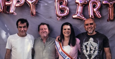 Three middle-aged siblings and their father standing with Happy Birthday balloons behind them