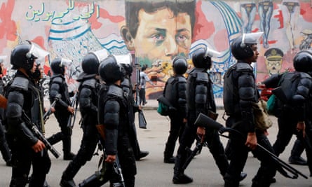 Riot police walk in front of graffiti, Cairo.