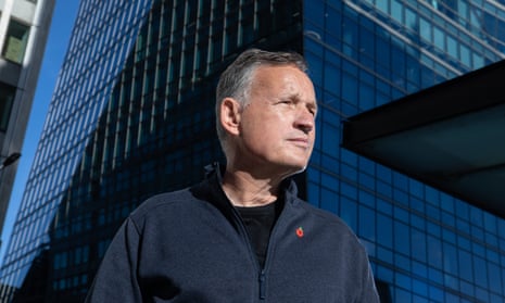 Portrait of Antony Jenkins in a grey zip-up fleece with the backdrop of a high-rise office building with a dark blue glass facia