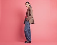 A model wearing a brown jacket and jeans, against a pink background