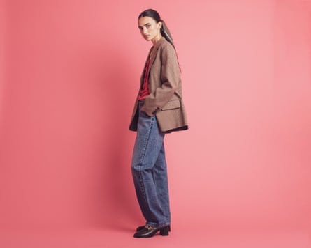 A model wearing a brown jacket and jeans, against a pink background