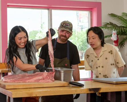 Awkwafina grimaces lifting a raw rib cut as Andrew Samia and Jimmy O. Yang watch.