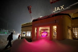 People walk towards the diner at night. Snow is piled in front of the one-storey building, which has a neon 'open' sign in the window