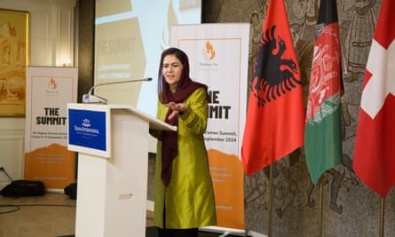 A woman in a black headscarf speaks at a podium.