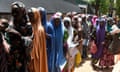Women carrying children queue outside a clinic
