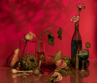 A still life image with a red background of flowers in glasses and bottles