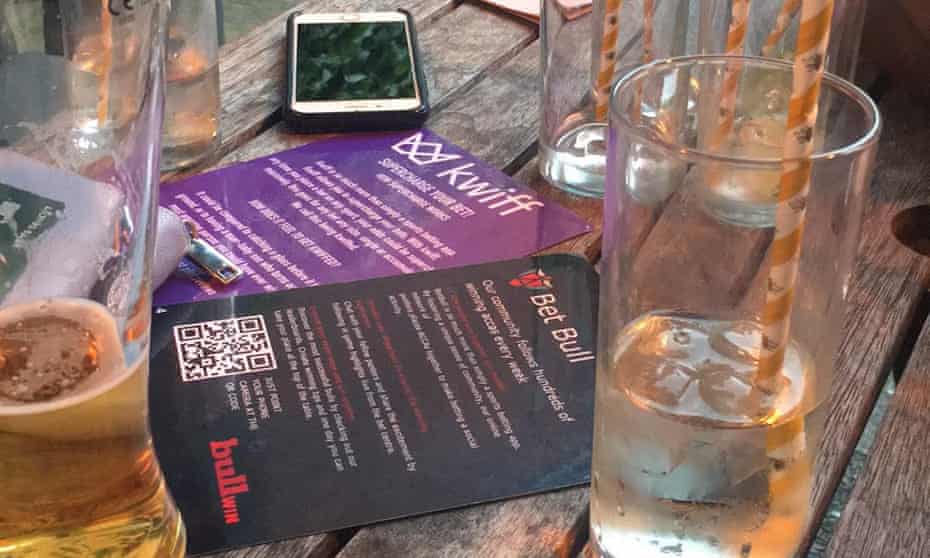Kwiff and BetBull gambling flyers on a pub table with mobile phone and half empty glasses.