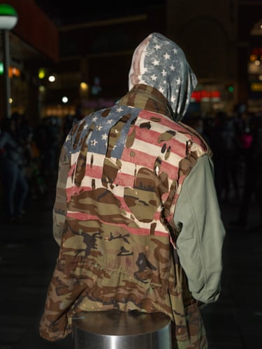 Flags, New York City, 2020. Young man seen from behind in a camouflage jacket, with a broken starts and stripes draped over it