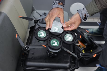 Hands can be seen putting a round dish into place on a black and orange drone.