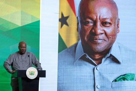A man stands at a podium, in front of a large image of himself