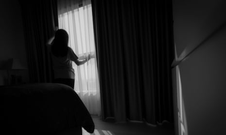 A young woman silhouetted at a window in a cuertained woman
