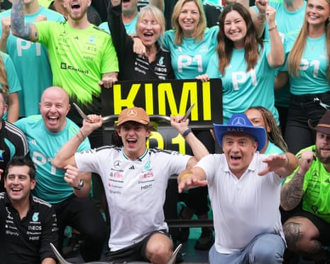 Kimi Antonelli celebrates winning, fists raised, as his F1 team cheers around him.