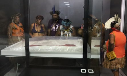 people in ceremonial clothing standing around a glass case with a cloak in it