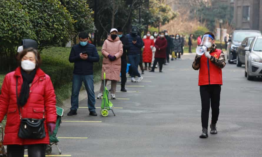 A community volunteer uses a megaphone to remind residents to maintain their social distance as they queue to collect their daily necessities outside a residential block in Xi'an.