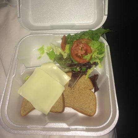 Polystyrene box containing two slices of bread and cheese, and a bit of tomato and lettuce