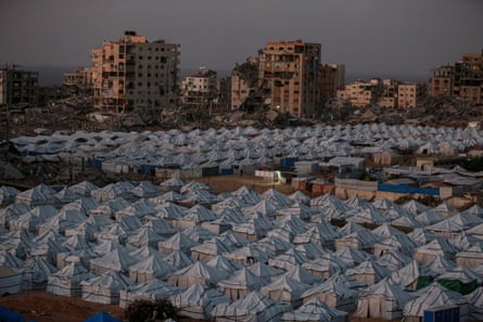 Mass of tents in Gaza with bombed out housing in the background