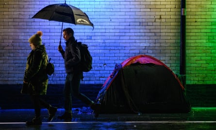 Commuters walk past the tent of a homeless person in London