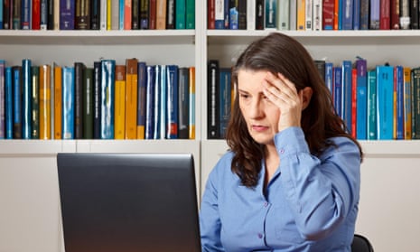 Mature woman in front of a computer in the office pressing a hand at her forehead.