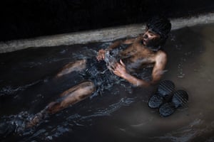 A reveller covered in black greasepaint lying in a pool of water