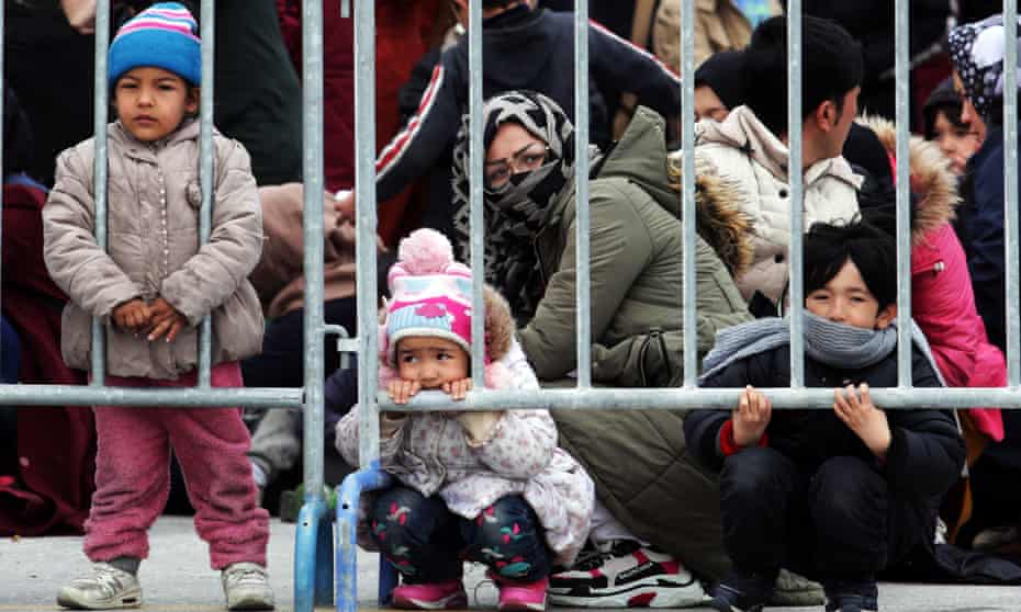 Children and other asylum seekers wait behind bars in Mytilene, Lesbos