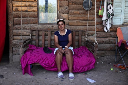 A woman sits on a swing bench outside a wooden house