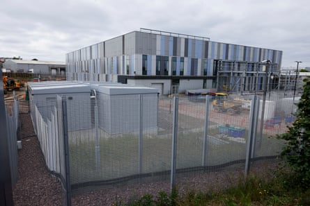 A square industrial unit with grey and pale blue panelling behind a wire fence.
