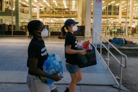 two women wearing face masks carrying supplies
