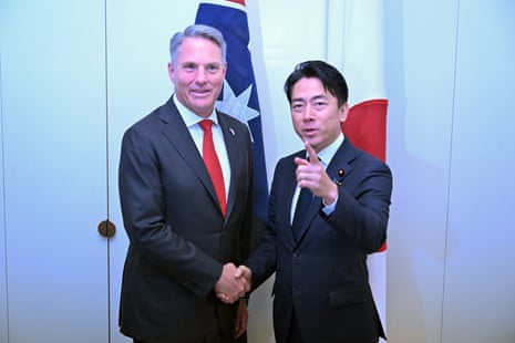 Richard Marles and Shinjirō Koizumi shaking hands and posing for the camera in front of the flags of Australia and Japan
