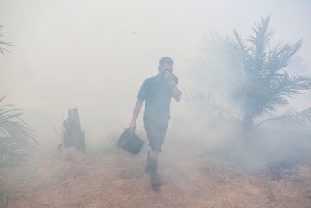 A man carrying a water bucket walks as wildfires get closer to his house