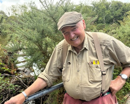 A smiling man in a flat cap in front of a wooded landscape