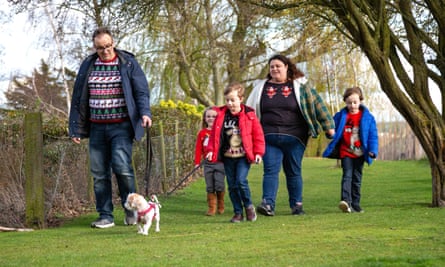 Family in Christmas jumpers walking a dog outdoors.