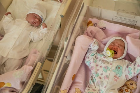 Two babies in hospital cots. The one on the left is asleep, while the other is crying