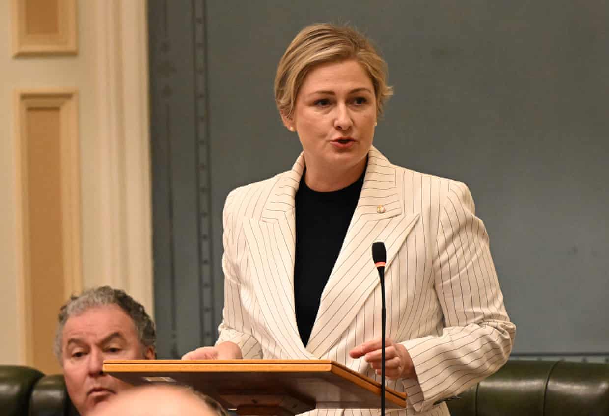 Woman with short blonde hairs wearing a white pinstripe jacket stands at a lectern