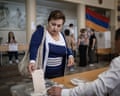 A woman places a ballot into a transparent ballot box at a polling station