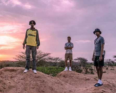 Three young men standing on mounds of earth with a sunset behind them
