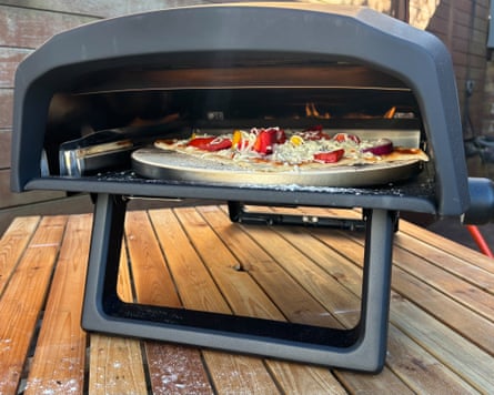 A salami pizza cooking in the ProCook Outdoor Pizza Oven, while the oven is on a wooden outdoor table.