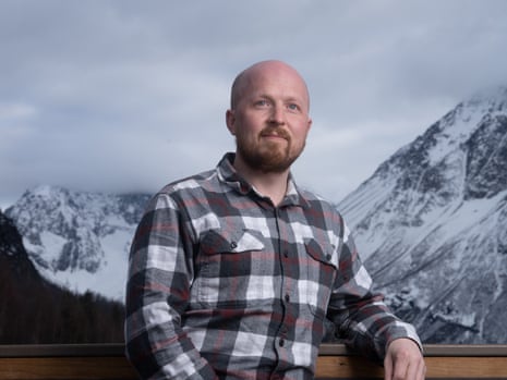 Jonathan Kreiss-Tomkins, bald with a beard, sits in a plaid shirt before snow-capped mountains
