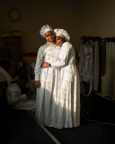 Sarah and Rachel, 2025Pictured here in Pentecostal dress after a Sunday service, Sarah (left) and her cousin Rachel embrace, illuminated by the golden light streaming in through the church window. Rachel’s smart watch adds a touch of modernity to this otherwise timeless image. Rachel invited the British photographer to visit her church, the Celestial Church of Christ, in their local area of Elephant and Castle. The portrait forms part of a wider series documenting the communities of south London and the spaces in which they gather