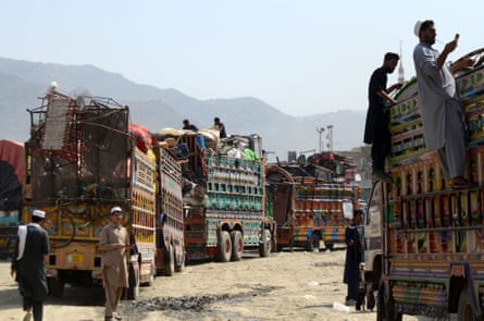 Brightly painted trucks piled high with household goods wait in a line as men mill about