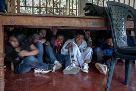 Children find shelter under a table during a mock evacuation after a possible bomb explosion or gunshot attack