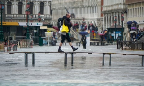 A man walks across an improvised bridge over a flooded Venice street