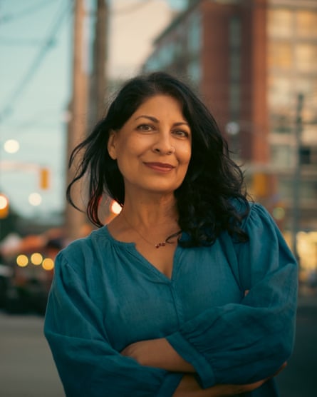 A middle-aged south Asian woman photographed on a street smiles at the camera