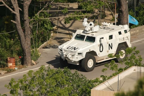 A white armoured United Nations Interim Force in Lebanon vehicle drives down a road, a bright blue UN flag waving from the back.