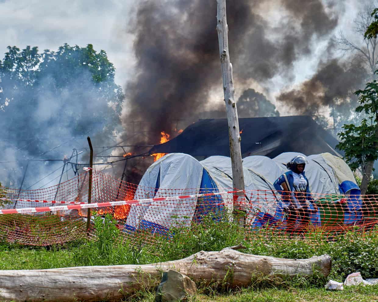 Smoke rises from a building, with tents and a plastic cordon in the foreground