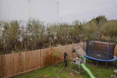 Dale Johnston watering a little tree in his back garden, with a massive datacentre beyond the fence