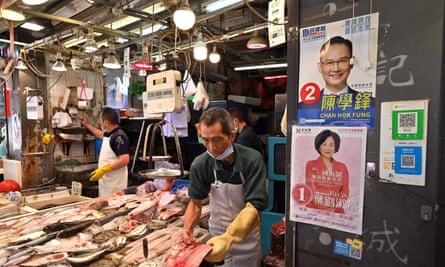 Fishmongers work next to campaign posters on the wall at a market in Hong Kong
