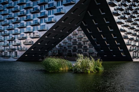 External shot of a vast modern building with balconies overlooking the water that the building is surrounded by
