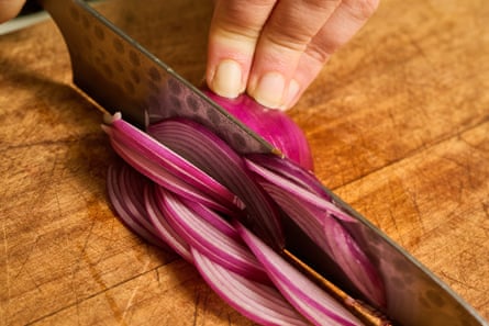 Close up of a hand slicing into a red onion.