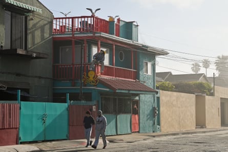Two people walk down a quit road alongside teal and read two-story buildings.
