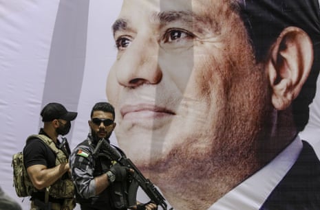 Two members of the Egyptian security forces stand guard beside a banner showing a photo of President Abdel Fatah al-Sisi.